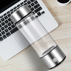 Clear glass water bottle with stainless steel base and lid, on desk beside laptop
