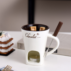 White chocolate fondue mug with candle base, chocolate pieces, and fondue fork, perfect for cozy desserts.