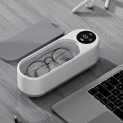 Compact ultrasonic cleaner with digital display cleaning glasses on wooden desk beside laptop