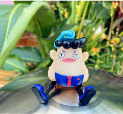 Funny cartoon figurine with blue hair and tie, sitting outdoors on metal surface