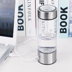 Portable hydrogen water generator bottle charging on desk with laptop and books