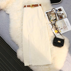 Cream corduroy skirt with front slit, brown belt, and black quilted bag on faux fur