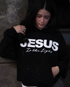 Woman wearing black hoodie with 'JESUS Is the Light' text, sparkly design, casual style