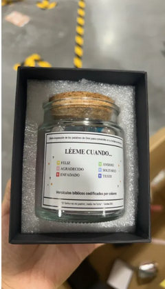 Glass jar with colorful biblical verses, labeled 'Léeme Cuando' for emotional support, nestled in foam packaging.