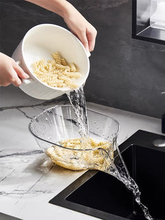 Clear glass pasta strainer bowl draining cooked rotini noodles in kitchen sink