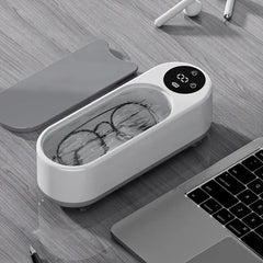 Ultrasonic cleaner with glasses inside, digital display, on desk near laptop and earbuds