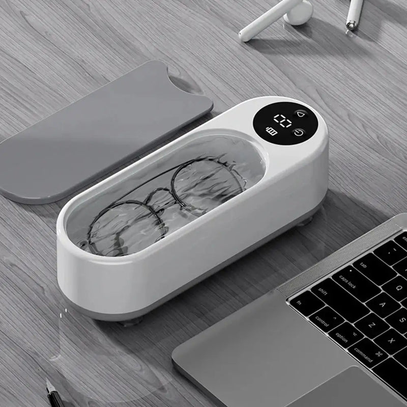 Ultrasonic cleaner with glasses inside, digital display, on desk beside laptop and earbuds