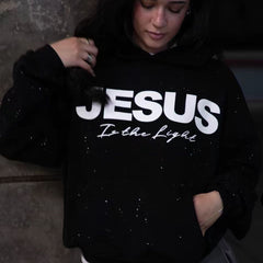 Black hoodie with 'JESUS Is the Light' text, sparkly details, worn by woman