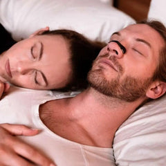 Couple sleeping peacefully in bed, man using nasal strip for better breathing